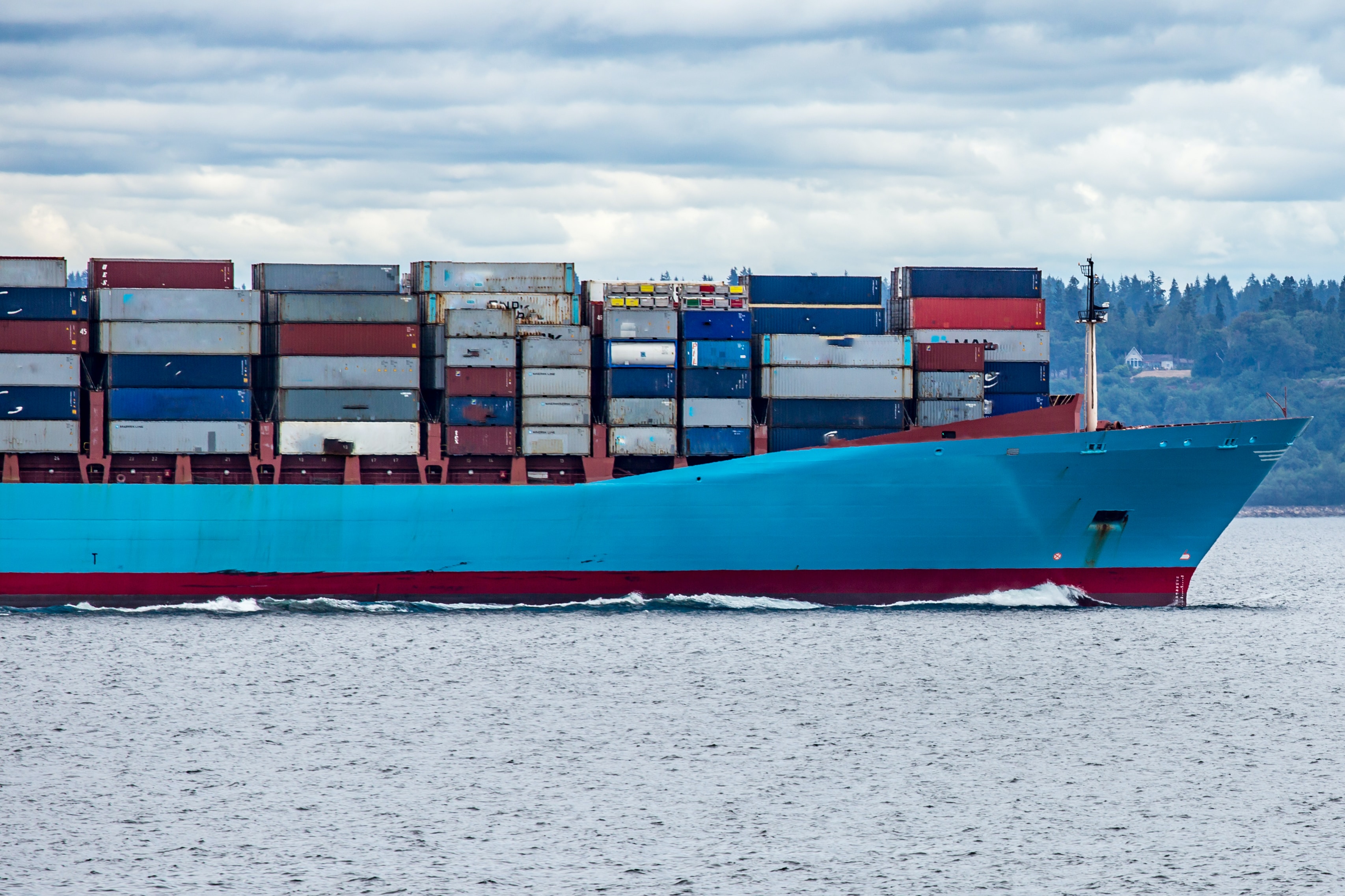Blaues, beladenes Containerschiff von links ins Bild kommend im Anschnitt